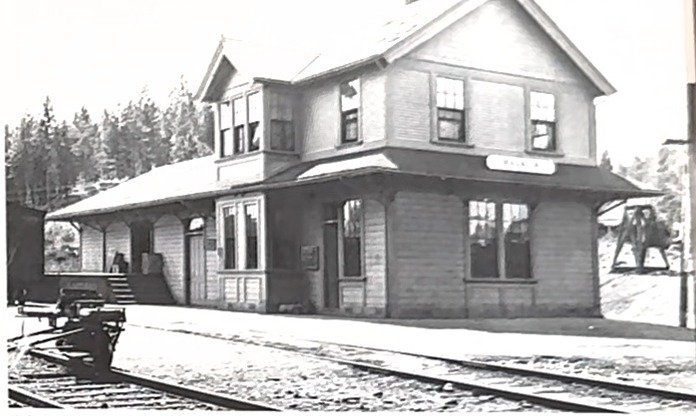 The photograph as cut from the page: a two-storey wooden depot beside railroad tracks